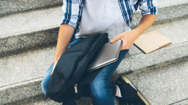 Cropped image of student putting laptop and textbook in his bag; Shutterstock ID 1141847237; Purchase Order: -