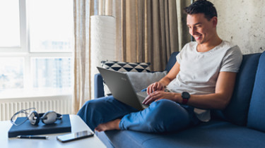young attractive man sitting on sofa at home working on laptop online, using internet, smiling, happy mood, freelancer, free leisure time, relaxed, modern job lifestyle; Shutterstock ID 1171675408; Purchase Order: -